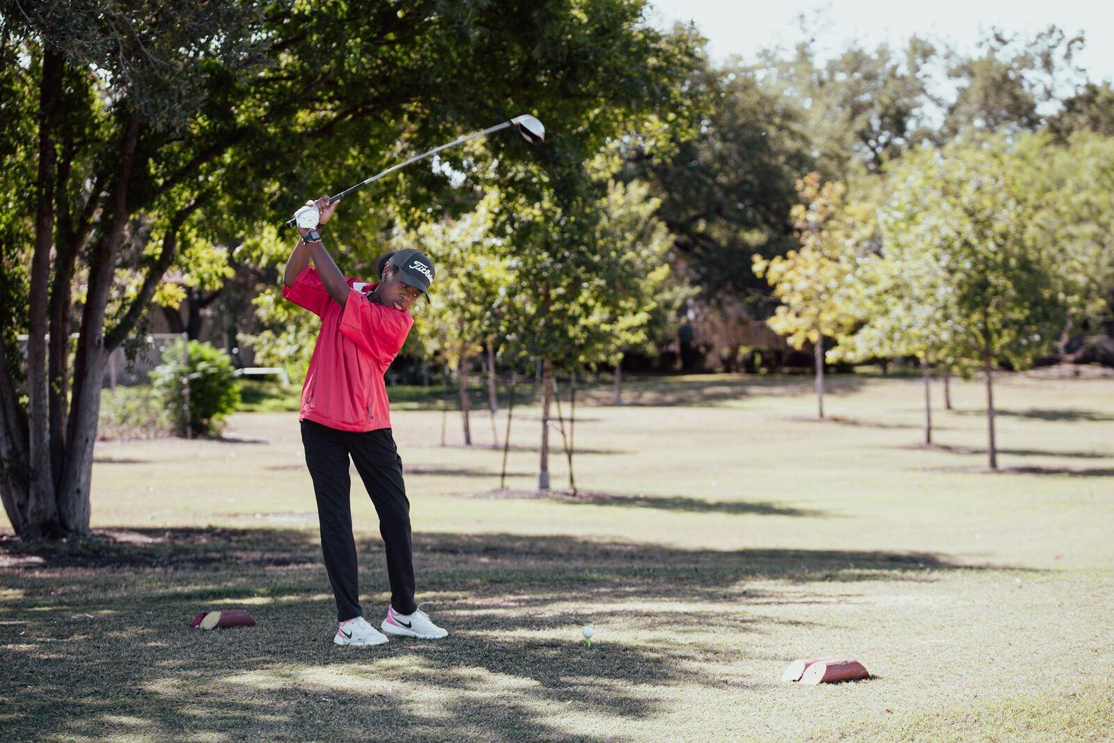 Junior golfer finishing a tee shot on a tree-lined course